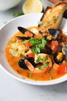 a white bowl filled with seafood and mussels next to bread on a table