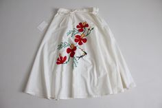 "Vintage 1970's crisp white cotton circle skirt with bright embroidered red floral motif, a high-wrap tie waist, and voluminous and flouncy sweep. Some discoloration to the waistband, please see last photo for your discretion! Fits Like: Small/Medium | No Label Size Circa 1970s Material: 100% cotton Condition: great! Measurements: 26-28\" waist | full hips | 29\" length" Vintage Floral Embroidery Summer Skirt, Retro White Skirt For Spring, White Flared Skirt With Floral Embroidery, White Cotton Wrap Skirt For Summer, White Embroidered Full Skirt, White Flared Wrap Skirt For Summer, White Retro Full Skirt, Retro White Full Skirt, Red Floral Embroidery Skirt For Spring