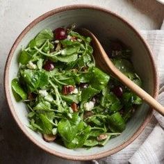 a bowl filled with greens and cherries on top of a white table cloth next to a wooden spoon