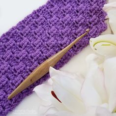 a purple crochet bag with a wooden handle next to white flowers and petals