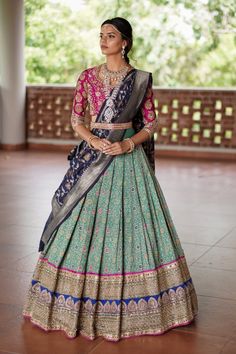 a woman in a blue and pink lehenga standing on a tile floor with trees in the background