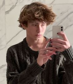 a young man taking a selfie in front of a marble wall with his cell phone