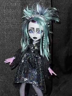 a doll with green hair and blue eyes wearing a black dress on a dark background