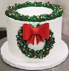 a decorated christmas cake sitting on top of a white plate with red bows and holly wreaths