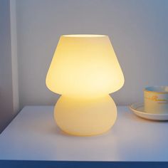 a white lamp sitting on top of a table next to a cup and saucer