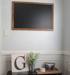 there is a blackboard on the wall above a desk with a potted plant