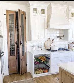 a kitchen with white walls and wooden floors, two doors open to reveal the pantry