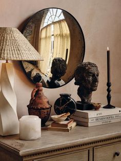 a table topped with books and a mirror next to a lamp on top of a dresser