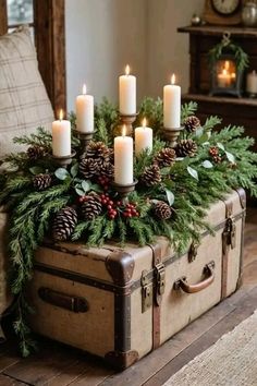 an old suitcase is adorned with pine cones and evergreen branches, candles and holly wreaths