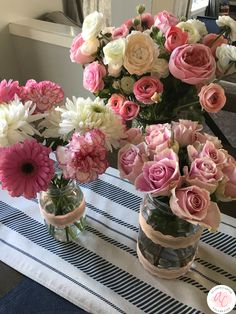 three vases filled with pink and white flowers on a striped table cloth next to a window