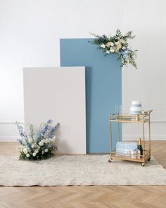 a table with flowers and candles on it in front of a blue wall next to a gold cart