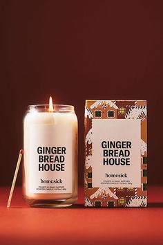 a ginger bread house candle next to a box on a red surface with a wooden stick