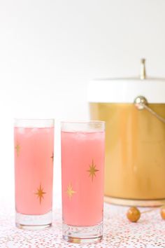 two glasses filled with pink liquid sitting on top of a table next to a pot