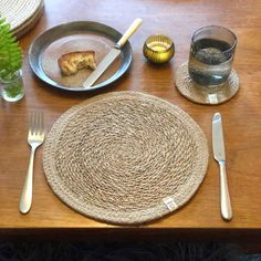 a place setting with silverware and plates on a wooden table top, along with a plant in a glass vase