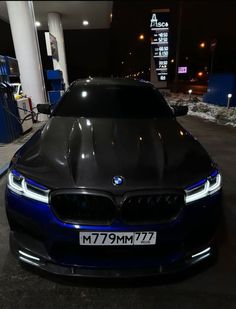 a blue bmw car parked in front of a gas station at night with its hood up