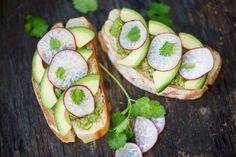 two pieces of bread with avocado and radishes on them, sitting on a wooden surface