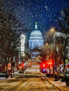 a snowy street with lights and buildings in the background