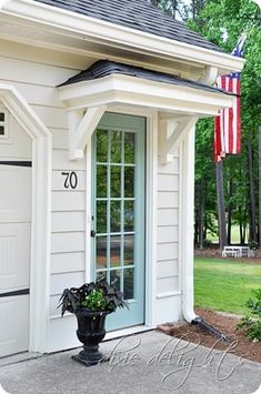 a white house with an american flag on the front door and side window, next to a potted plant