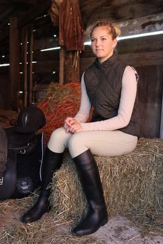 a woman sitting on top of hay next to a horse saddle and rider's bag