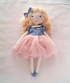 a doll with blonde hair wearing a pink and blue dress on a white sheeted surface