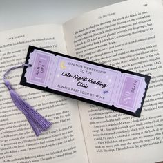 an open book with a tassel on top of it next to a purple ribbon