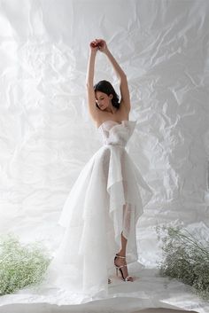 a woman in a white dress is posing for a photo with her arms up and hands behind her head