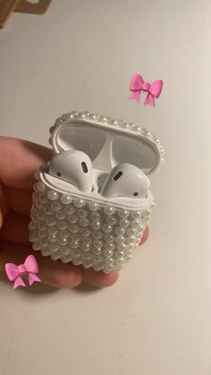 a hand holding an airpods case with two ears in it and pink bows on the side