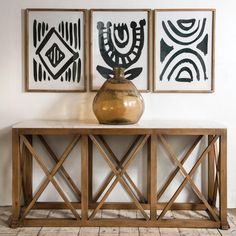 a vase sitting on top of a wooden table in front of two framed art pieces