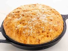 a baked bread in a black cast iron skillet on a white counter top,