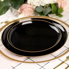 a black plate with gold trim sits on a white tablecloth next to pink and white flowers