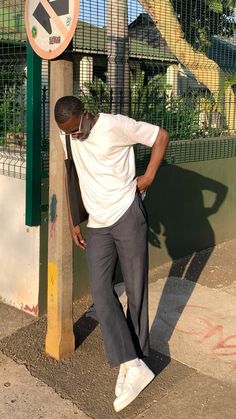 a man leaning against a pole with his hand on his hip and looking at the ground