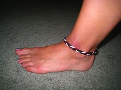 a woman's bare foot wearing a black and white braided ankleband with pink toenails