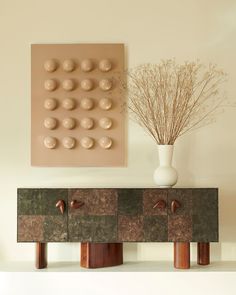 a vase sitting on top of a wooden shelf next to a wall mounted art piece