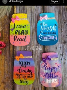 four painted mason jars with sayings on them sitting on a wooden table next to flowers