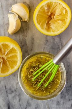 lemons, garlic and herbs in a jar with a whisk on the side