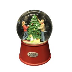 a snow globe with two people decorating a christmas tree in it's center