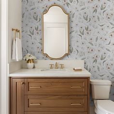 a white toilet sitting next to a bathroom sink under a mirror on top of a wooden cabinet