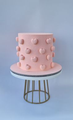 a pink cake sitting on top of a white table next to a metal stand with polka dots