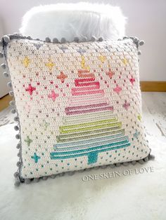 a crocheted pillow with a rainbow cake on it and white furnishing