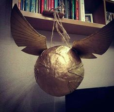 a metal ball with wings hanging from it's side in front of a bookshelf