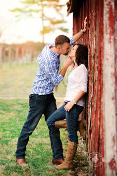 a man and woman leaning against a red barn