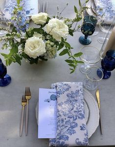 the table is set with blue and white plates, napkins, silverware, and flowers