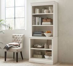 a white bookcase in the corner of a room with a chair and potted plant