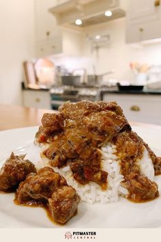 a white plate topped with rice and meat covered in sauce on top of a kitchen counter