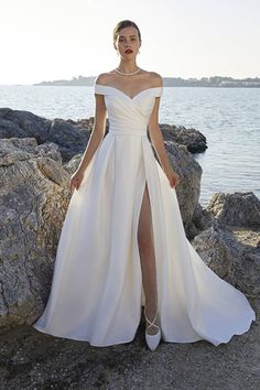 a woman in a white dress standing on rocks near the water with her legs crossed