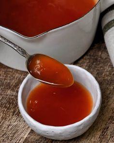 a spoon full of sauce sitting in a white bowl on top of a wooden table