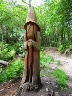 a statue of a man with a hat and beard is in the middle of a forest