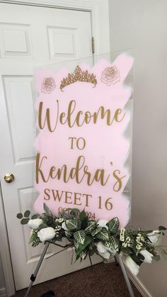 a welcome sign with flowers and greenery in front of a door that says, welcome to kendra's sweet 16