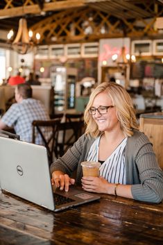 a woman sitting at a table with a laptop and coffee in front of her smiling