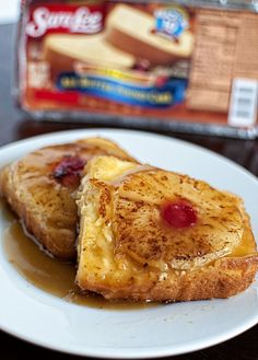 two pieces of french toast on a white plate with syrup and butter in the background